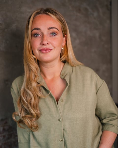 Portrait of a woman with long strawberry blonde hair wearing a sage green button-up shirt against a gray background