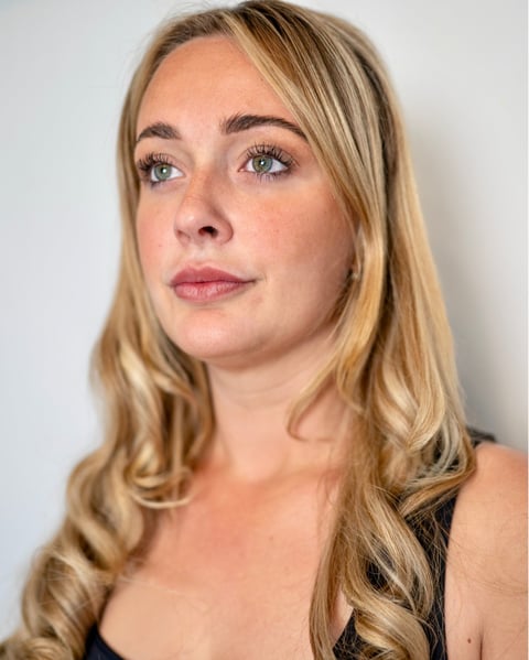 Portrait of a woman with long blonde wavy hair and neutral makeup, looking directly at camera